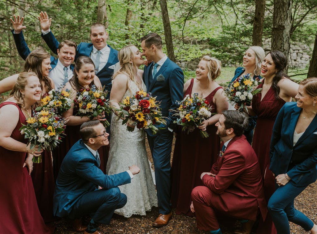 Brilliant Blue suits paired with rustic, deep red bridesmaids dresses. Groomswomen ad groomsmen in coordinating suits